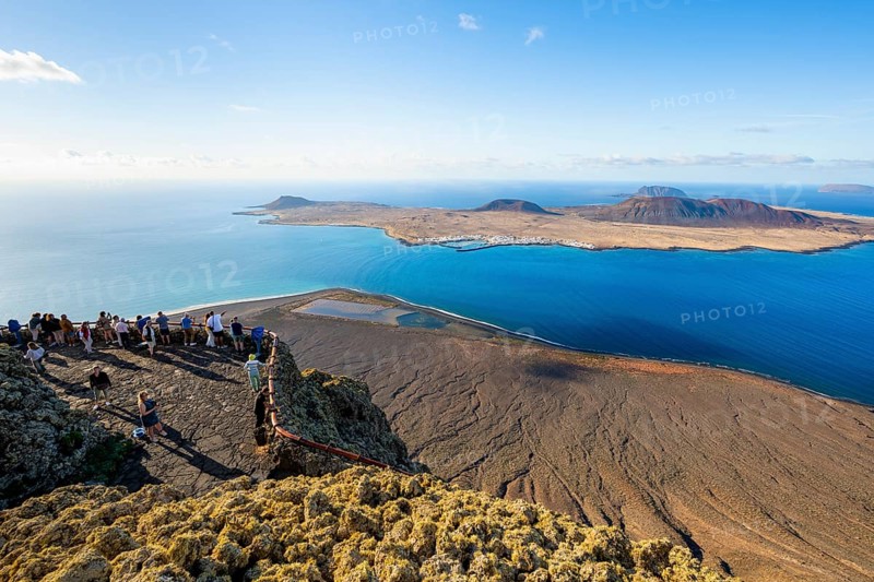 View of La Graciosa island with volcanic craters in the evening light, tourists on an observation deck at the Mirador del Río viewpoint designed by artist César Manrique, Lanzarote, Canary Islands, Spain