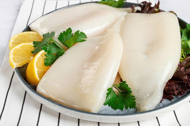 Fresh squid on a black plate with greens and lemon slices prepared for cooking in a kitchen setting