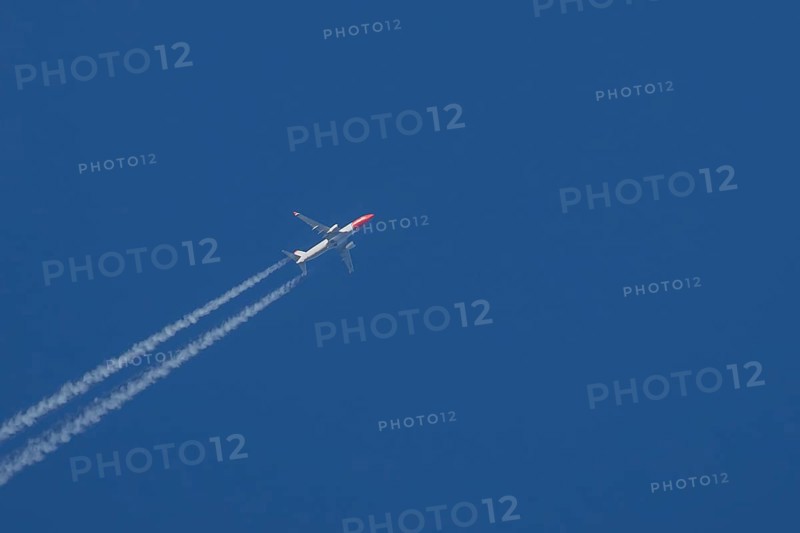 Boeing 737 jet passenger aircraft of Norwegian Air airlines flying in a blue sky with contrails or vapour trails behind, England, United Kingdom