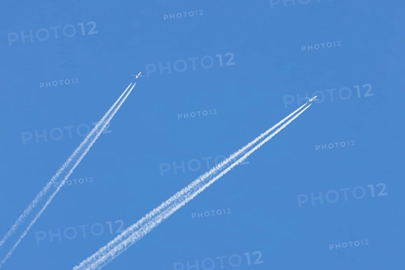Two jet passenger aircraft flying in a blue sky with contrails or vapour trails behind, England, United Kingdom