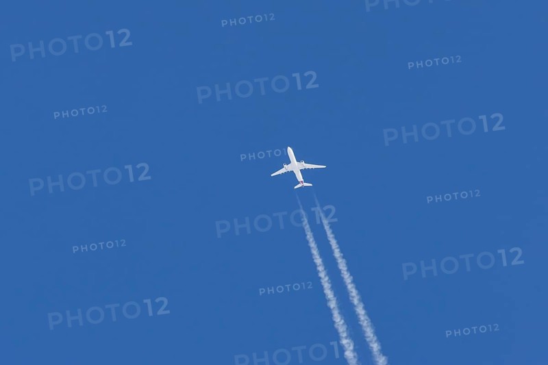 Jet passenger aircraft flying in a blue sky with contrails or vapour trails behind, England, United Kingdom