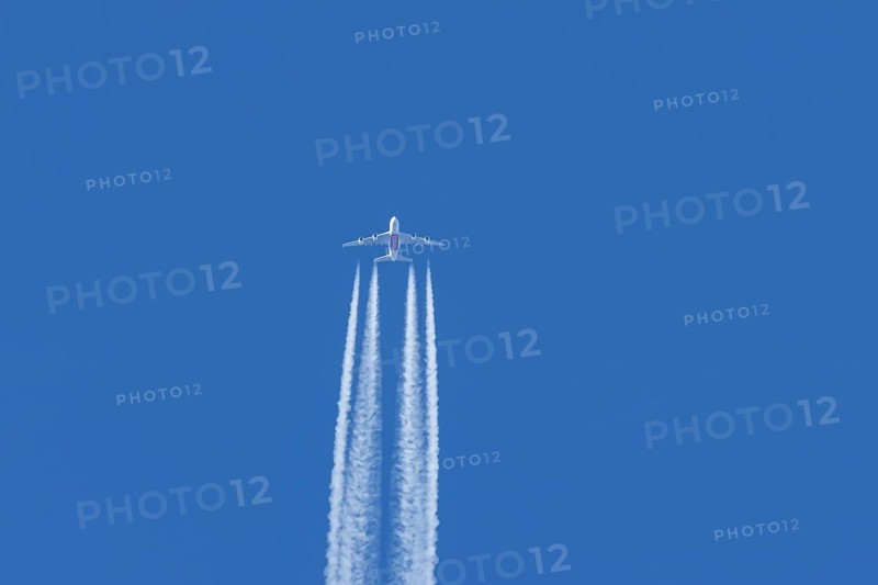Airbus A380 jet passenger aircraft of Emirates airlines flying in a blue sky with contrails or vapour trails behind, England, United Kingdom