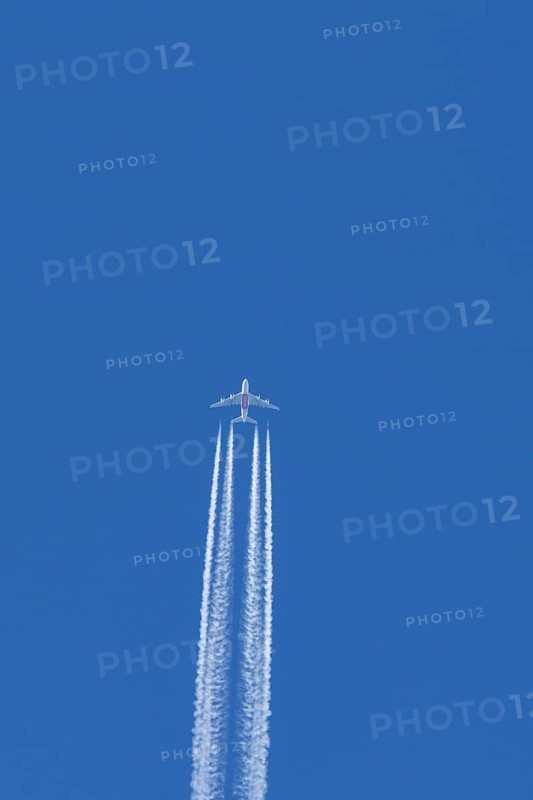 Airbus A380 jet passenger aircraft of Emirates airlines flying in a blue sky with contrails or vapour trails behind, England, United Kingdom
