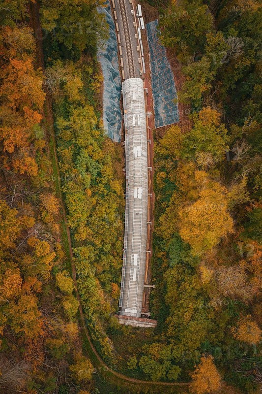 Aerial view of a partly covered railway tunnel surrounded by colorful trees, Hermann-Hesse-Bahn construction site, Calw, Germany