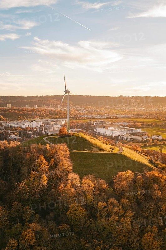 A wind turbine on a hill surrounded by autumn trees and urban landscape, Grüner Heiner, Korntal, Germany