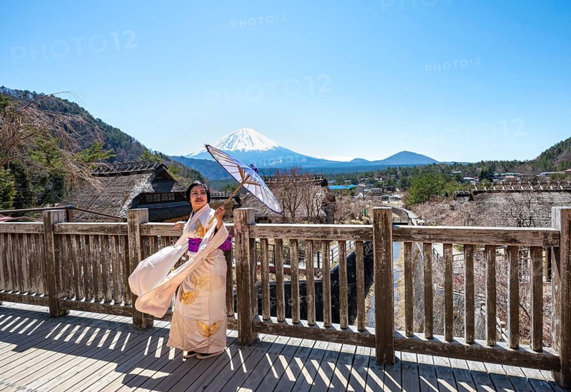 Japanese woman in kimono with umbrella, Iyashinosato open-air museum, old Japanese village with traditional houses, at the back volcano Mt. Fuji, Fujikawaguchiko, Saiko, Japón