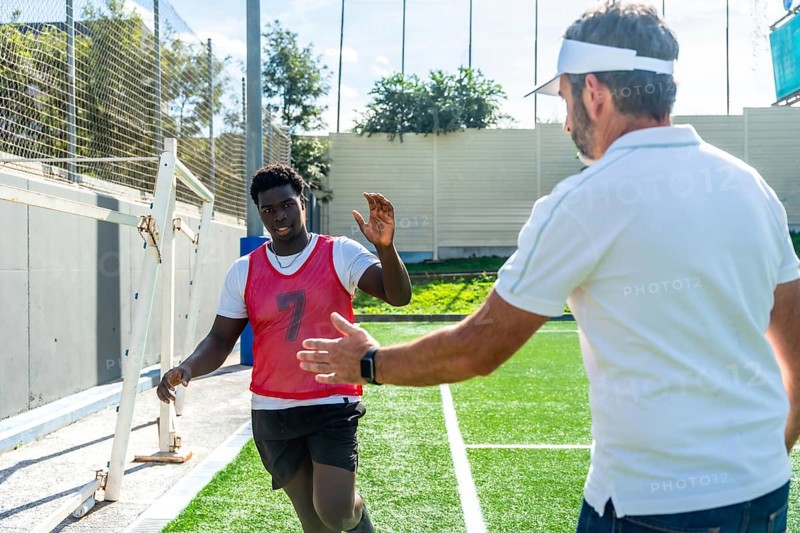 Young male soccer player high fiving his adult coach on an artificial turf sports field, symbolizing motivation, teamwork, and mentorship during a sports training session