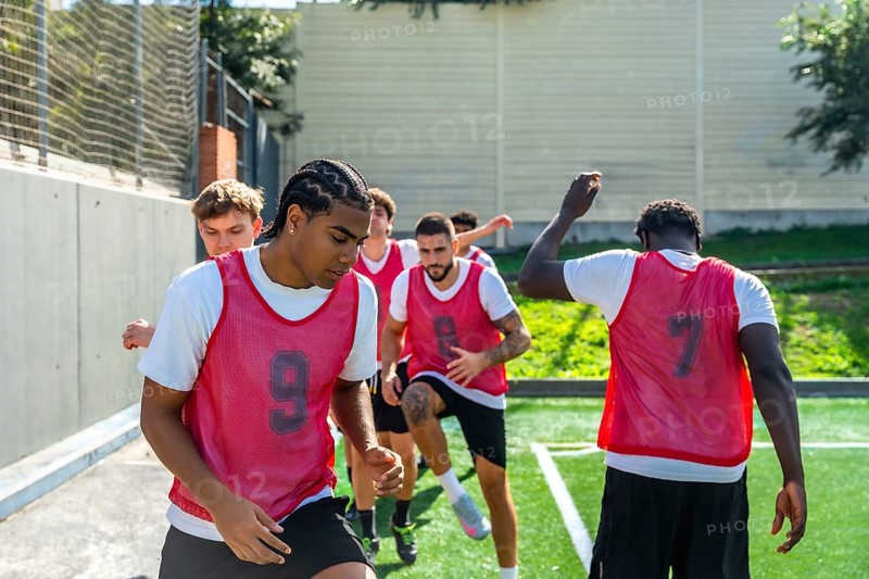Group of diverse male soccer players engaging in intense drills and warm up exercises on an artificial turf field, focusing on teamwork and athletic performance during practice