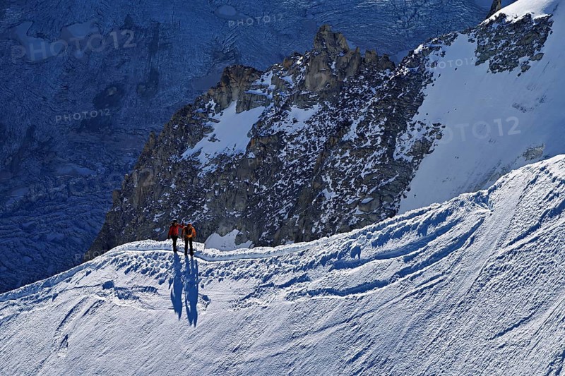 Two ascended mountaineers run across a snow-covered mountain ridge, Aiguille du Midi, Chamonix-Mont-Blanc, Haute-Savoie, France