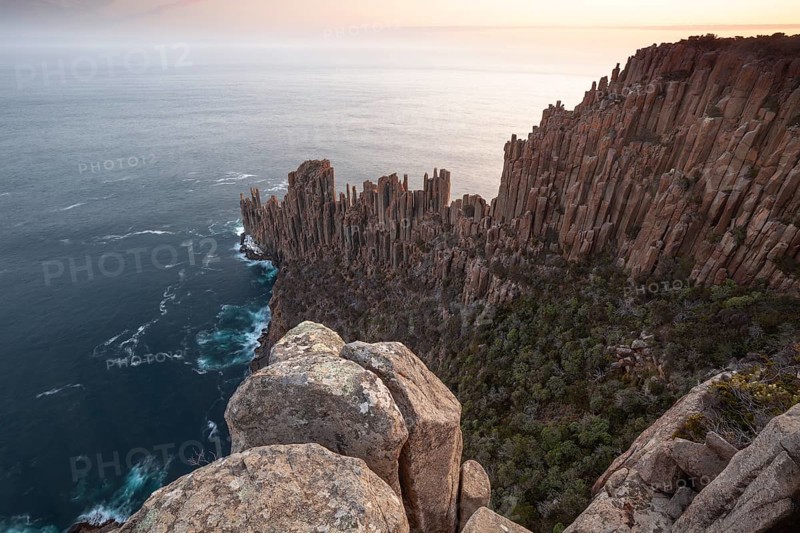 Long exposure shows sunset over the cliffs of Cape Raoul. Golden light hits the sea and colors the rocks warmly in the evening. Cape Raoul, Tasman Peninsula, Tasmania, Australia