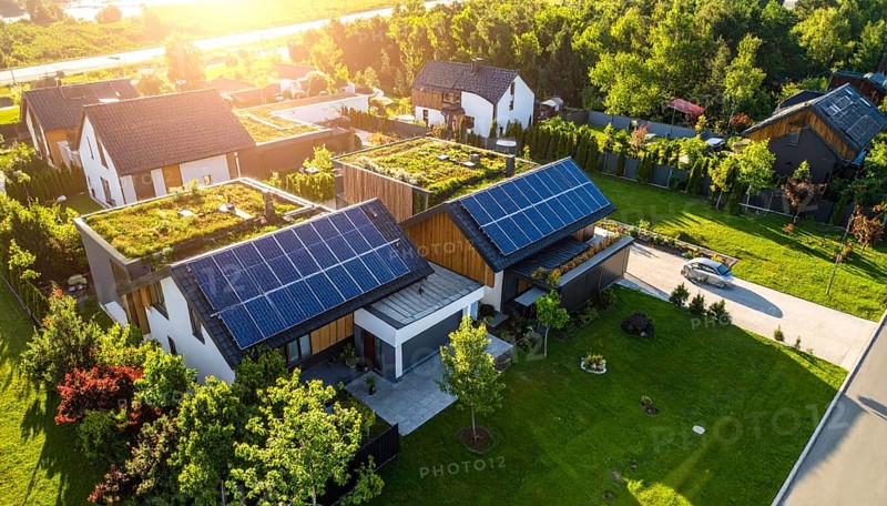 Aerial view showcases modern houses with solar panels and green roofs in a suburban setting, vibrant sunrise with blue sky, AI generated