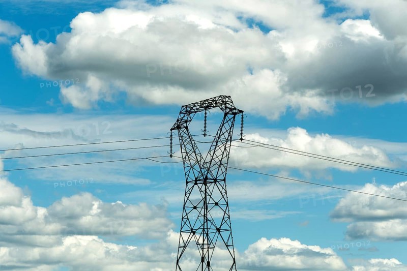 High voltage power lines against a bright blue sky with scattered clouds, Puy de Dome, Auvergne Rhone Alpes, France
