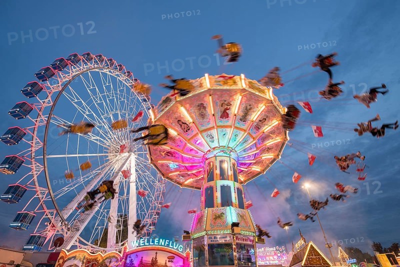 An illuminated chain carousel and Ferris wheel at night at a funfair, people swinging on chains, Bad Cannstatt, Stuttgart, Baden-Württemberg, Germany