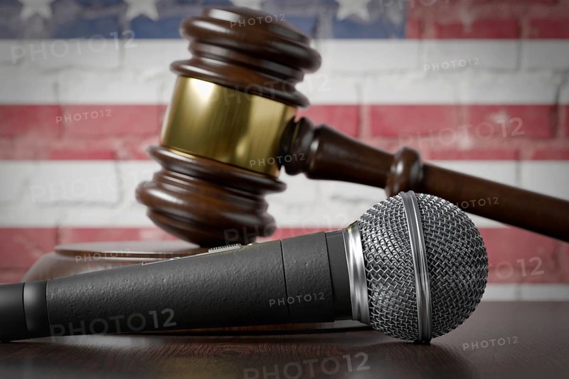 Microphone and gavel resting on a table with the american flag painted on A brick wall behind