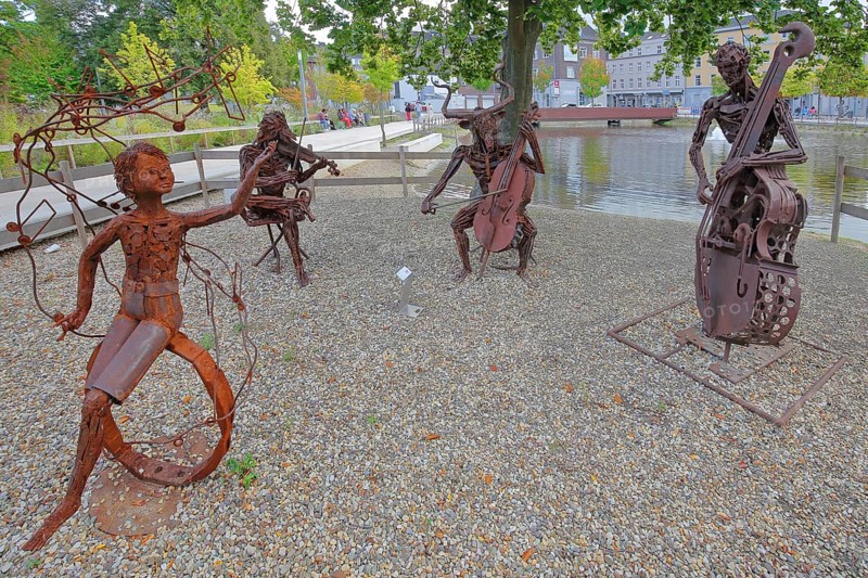 Sculpture The Concert by Günther Fahrner, rusty, metal sculpture, sheet metal, modern art, four bizarre whimsical musicians, trio, quartet, double bass player, violin player, cello player, string instruments, cello, violin, double bass, make music, musician, pond, bull figure, Bastinsweiher, Rhineland, Stolberg, North Rhine-Westphalia, Germany