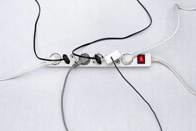 Top view of a power strip with on/off switch and various plugged-in plugs and cables on a white Resopal panel