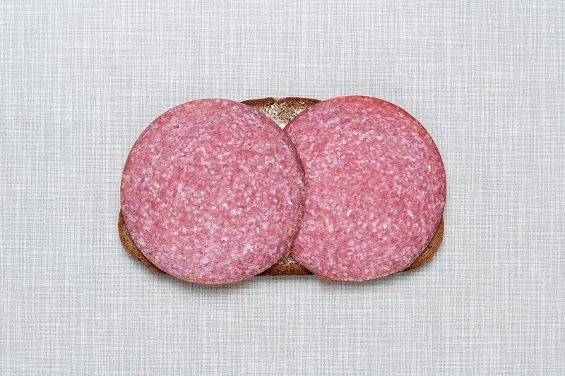 Top shot of a slice of bread smeared with margarine and topped with salami on a white Resopal plate