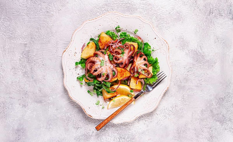 Grilled octopus with baked potatoes and fresh herbs, on a decorative light plate, homemade, no people