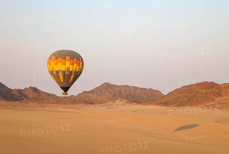 The hot-air balloon above an arid plain and isolated mountain ridges at the edge of the Namib Desert. Aerial view from a second balloon. Namibia
