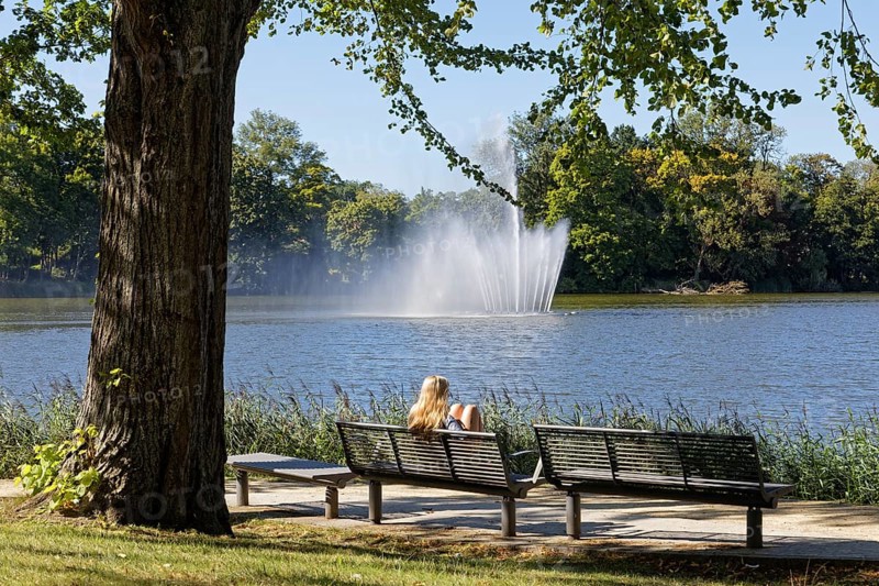 Blonde woman on park bench looking at fountain in Knieperteich Stralsund, Mecklenburg-Vorpommern, Germany