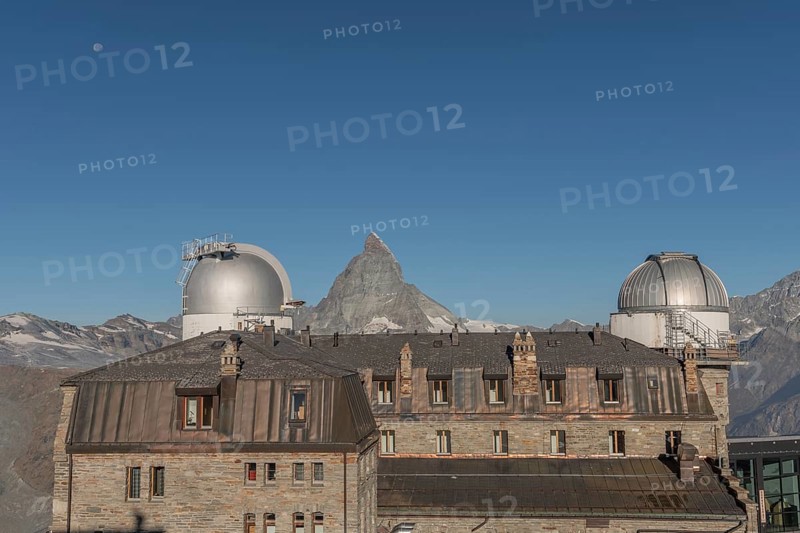 This breathtaking view shows the iconic Matterhorn mountain rising behind a historic observatory building. The clear blue sky enhances the serene atmosphere in autumn