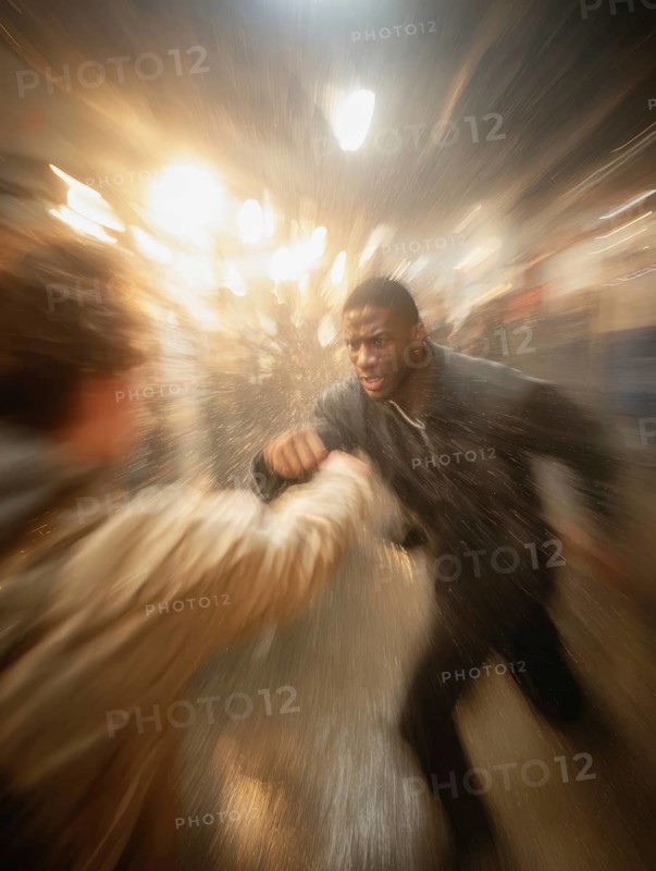 A man gets into a fighting stance, surrounded by dynamic movement and a background filled with lights, symbolic image for physical confrontation in public, use of force, physical violence, act of violence, aggressive behaviour, brawl, AI generated