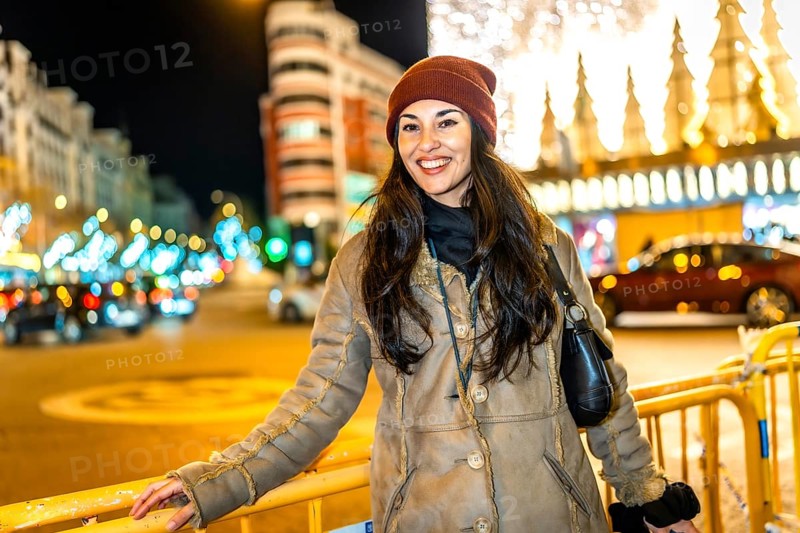 Young woman wearing winter clothes smiling in a city street decorated with christmas lights at night