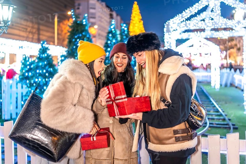Three happy women opening a christmas gift box at a decorated night market during winter holidays