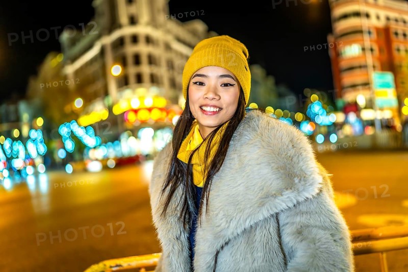 Asian woman wearing cozy winter clothes, smiling and enjoying the vibrant christmas lights illuminating the bustling city streets at night