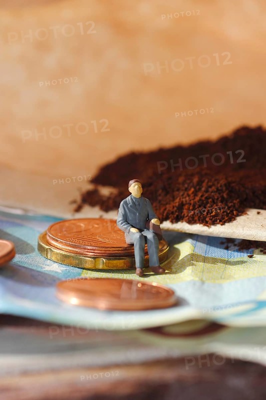 Miniature figure of a man sitting on coins and banknotes, ground coffee in a filter bag in the background, North Rhine-Westphalia, Germany