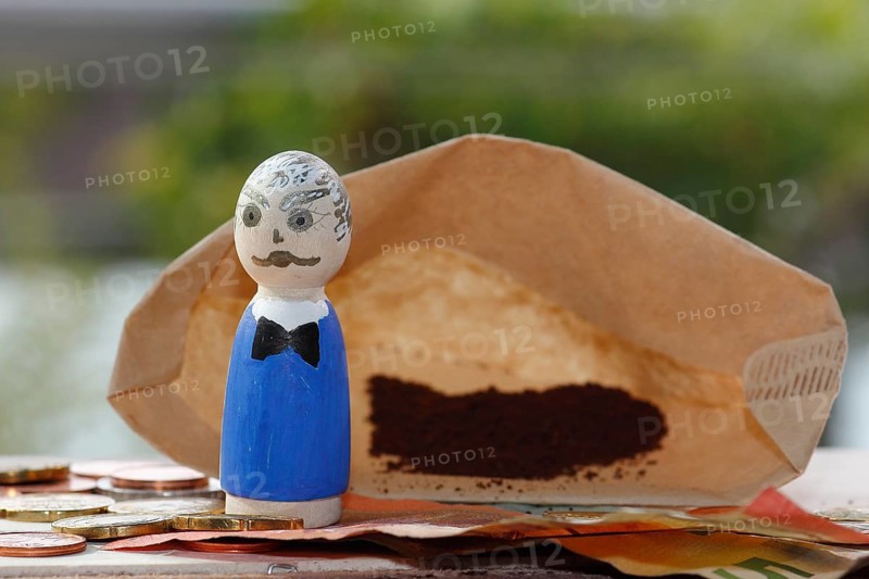 Male wooden cone figure with coins and banknote in front of filter bag with coffee North Rhine-Westphalia, Germany