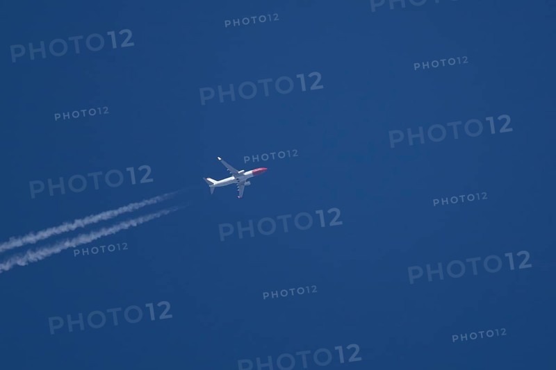 Boeing 737 jet passenger aircraft of Norweign Air with a vapour trial or contrail behind flying in a blue sky, England, United Kingdom
