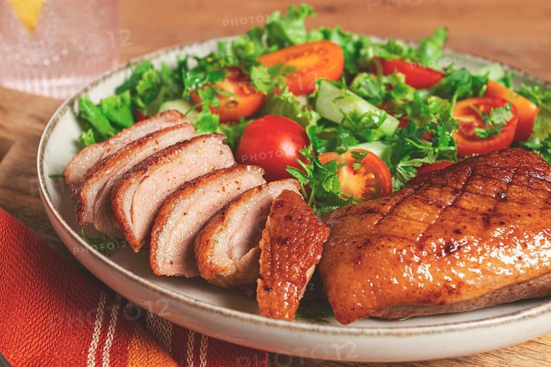 Delicious grilled duck breast served with fresh garden salad and cherry tomatoes at a rustic dining table