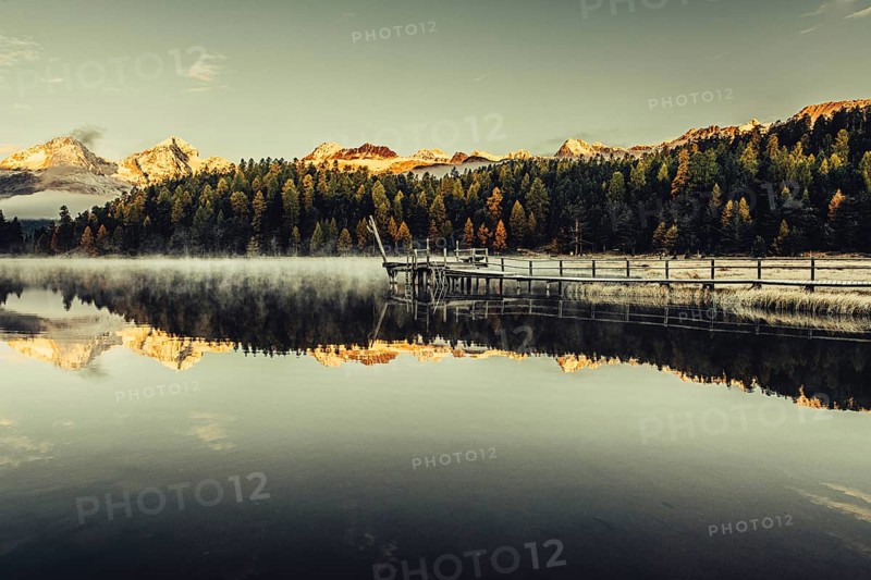 Lake Staz near Sankt Moritz in the Engadin in Switzerland. Morning atmosphere with fog in autumn. Water reflection and snow-covered mountains in the background