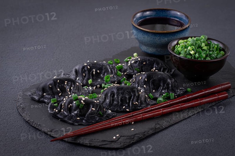 Japanese gyoza dumplings, made of black dough, black gyoza, with green onions and sauce, on a plate, close-up