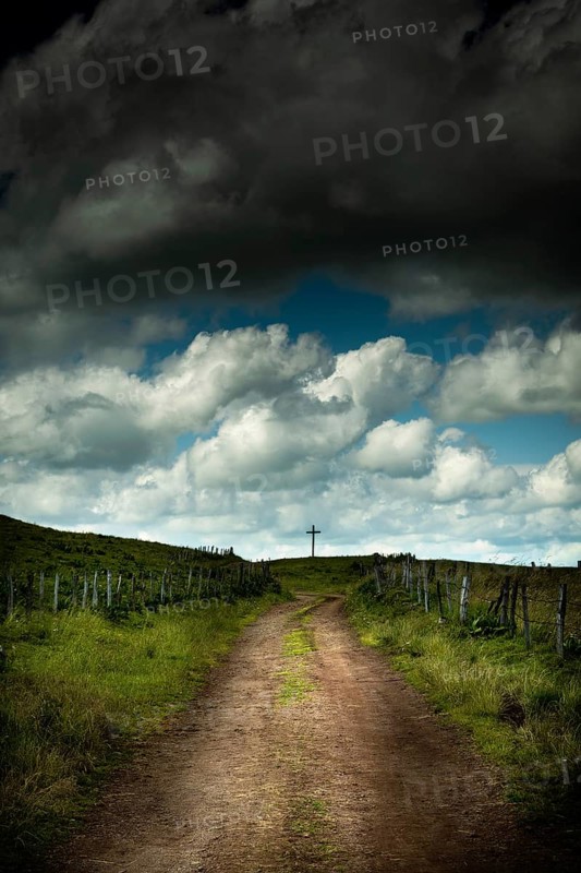 A winding dirt road leads the eye to a solitary cross. Cézallier, Auvergne Volcanoes Regional Natural Park, Puy-de-Dôme, Auvergne Rhone Alpes, France