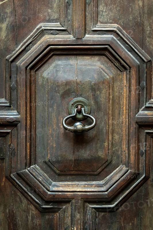 Intricate details on a weathered wooden door featuring an ornate, vintage knocker. The craftsmanship highlights the beauty of traditional architecture in an urban environment
