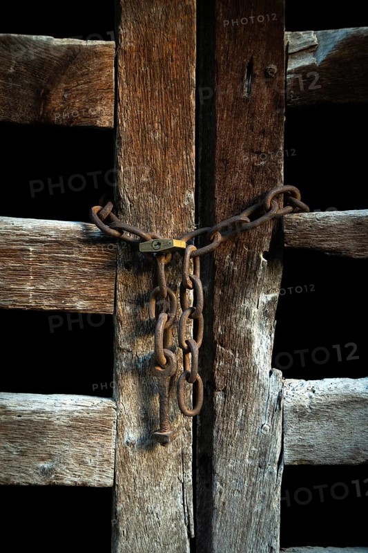 The wooden door, weathered and aged, is closed off with rusty chains, creating an intriguing contrast against the dark background, evoking a sense of mystery and history