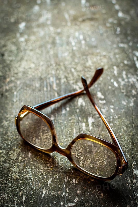 A pair of vintage glasses lies on a weathered wooden surface, enhanced by warm natural light reflecting off the delicate lenses, creating a serene atmosphere