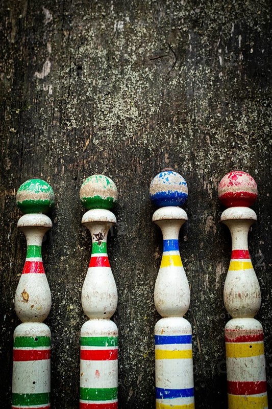 Vibrant wooden bowling pins stand aligned against a weathered surface, inviting players to enjoy a fun outdoor game with friends in a lively atmosphere