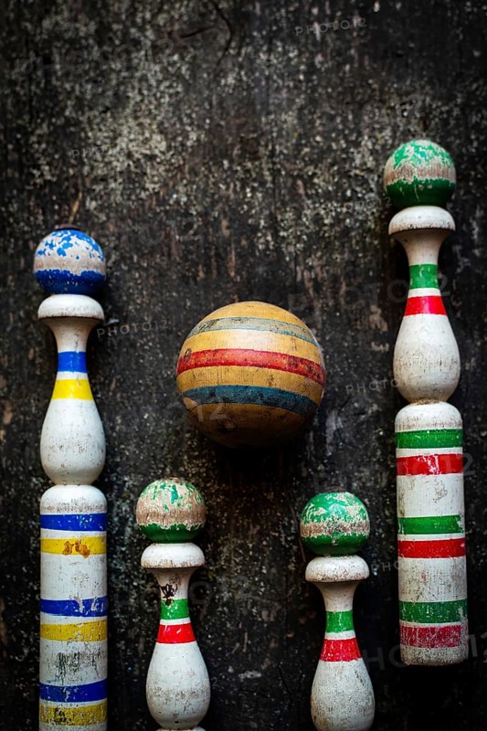 A classic bowling game set showcases worn wooden pins in vibrant colors and a striped ball, displayed on a rustic surface that enhances the nostalgic atmosphere for friendly competition