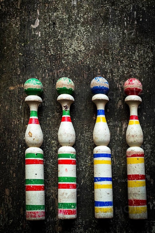 Four vintage wooden bowling pins with vibrant colors sit in a row on a rustic wooden surface, showcasing their charming, worn look in a cozy indoor ambiance