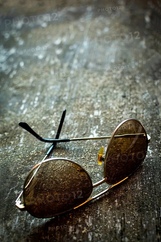 A pair of sunglasses lies on a rustic textured surface, capturing the essence of time. Warm light reflects off the lenses, enhancing the vintage atmosphere of the setting