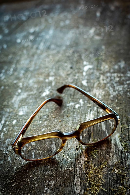 A pair of vintage glasses lies on a weathered wooden table. The unique design is illuminated by warm natural light, enhancing the serene ambiance of the setting