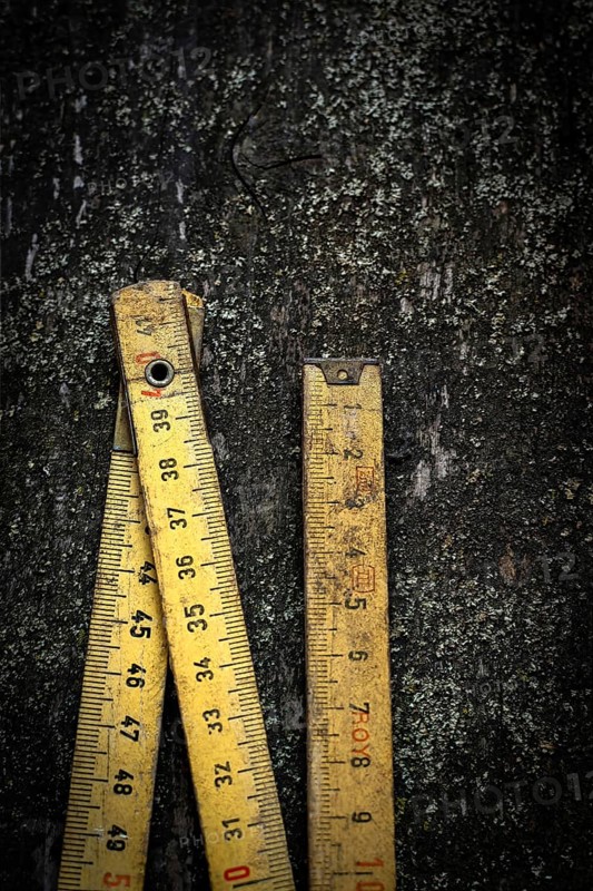 Two antique wooden rulers rest on a rough, dark surface, showcasing their intricate details and nostalgic wear, illuminated by scattered light reflections
