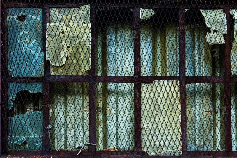 The weathered window features damaged glass and rusty metal bars, showing signs of decay and neglect in an abandoned structure. Peeling paint adds to the building's history