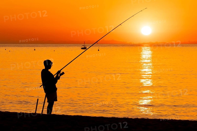 A boy fishing shortly after sunrise on the Costa Rei, a coastline of the Italian island of Sardinia, in the Mediterranean Sea, Monte Nai, Costa Rei, Sardinia, Italy
