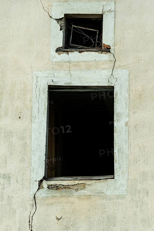 Cracked walls and dark empty windows show the neglect of an abandoned structure. The peeling paint suggests years of deterioration in an isolated location