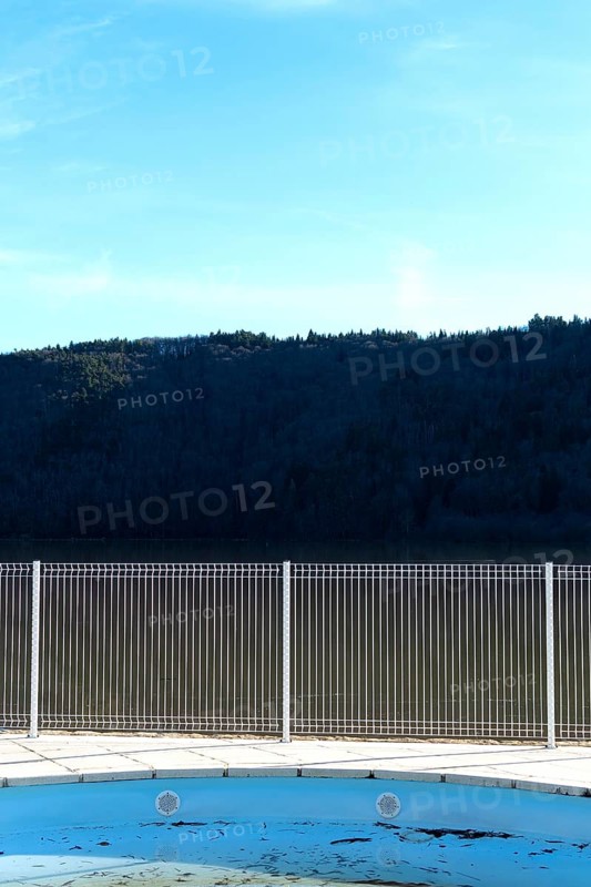 A swimming pool reflects the blue sky and surrounding mountains. A metal fence surrounds the space, accentuating the serene atmosphere during daylight