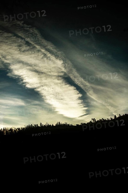 Cloud patterns swirl dramatically in the twilight sky, contrasting against the dark outline of a forest. The scene captures the beauty of nature at day's end